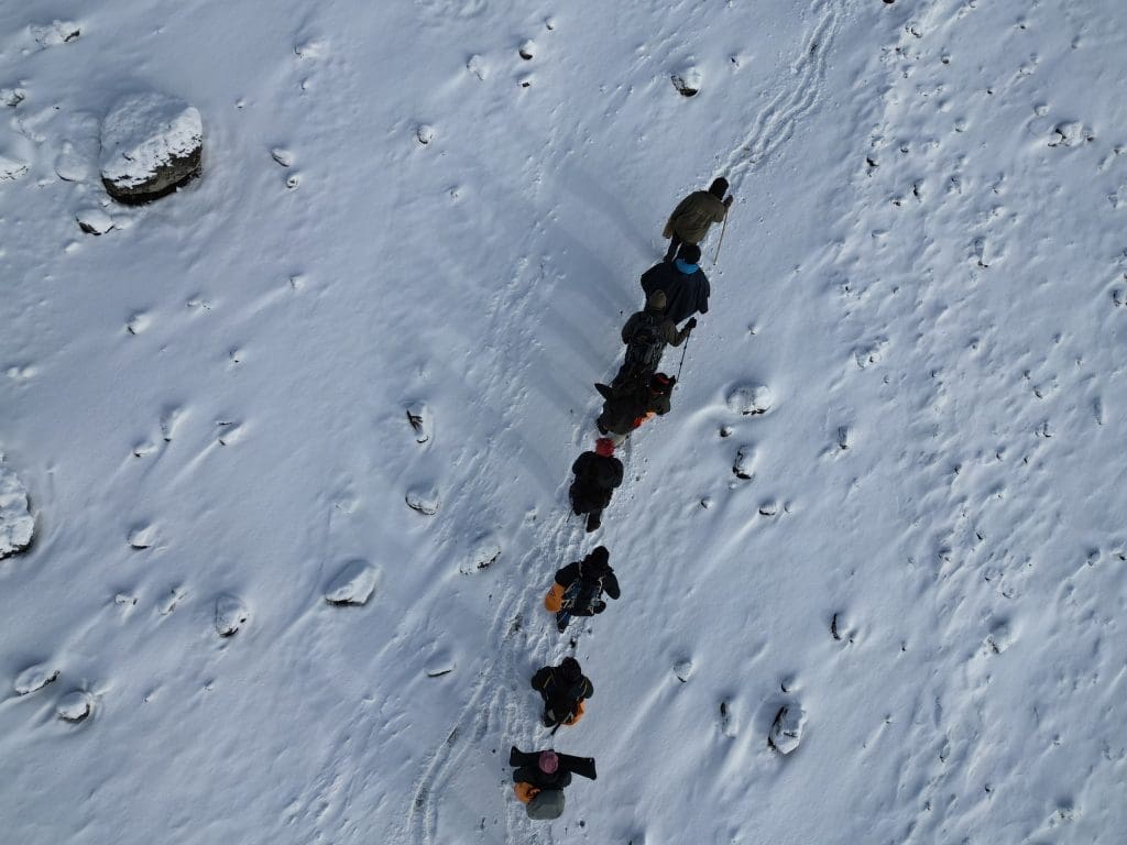 A group of climbers trekking through snow toward Mount Kilimanjaro’s summit from base camp.