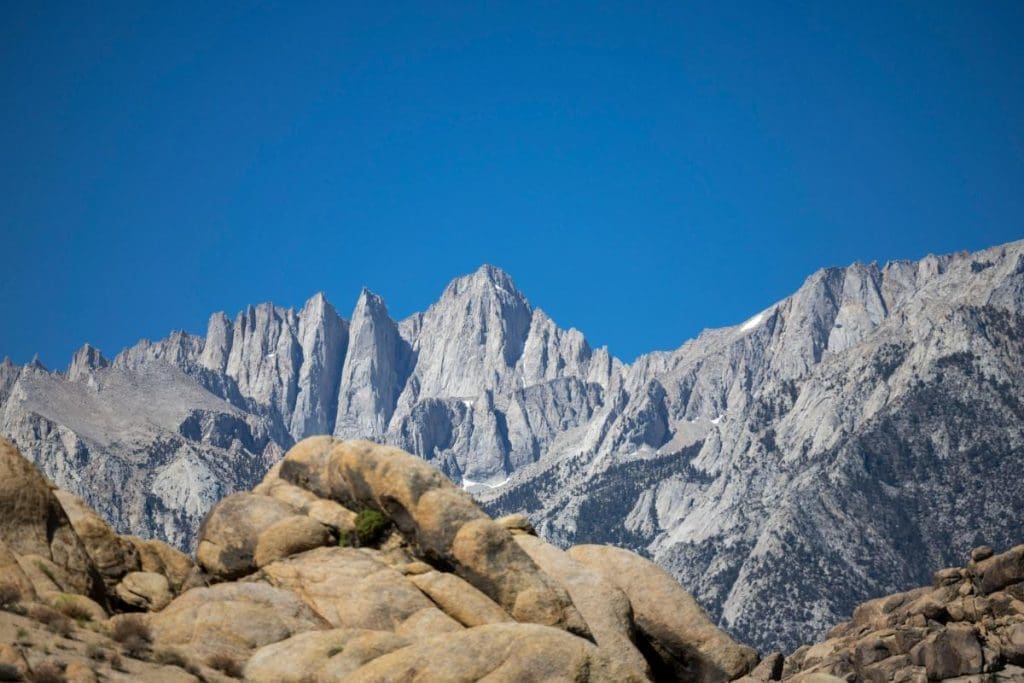 Rugged granite peaks of Mount Whitney under a clear blue sky, viewed from Alabama Hills in California.