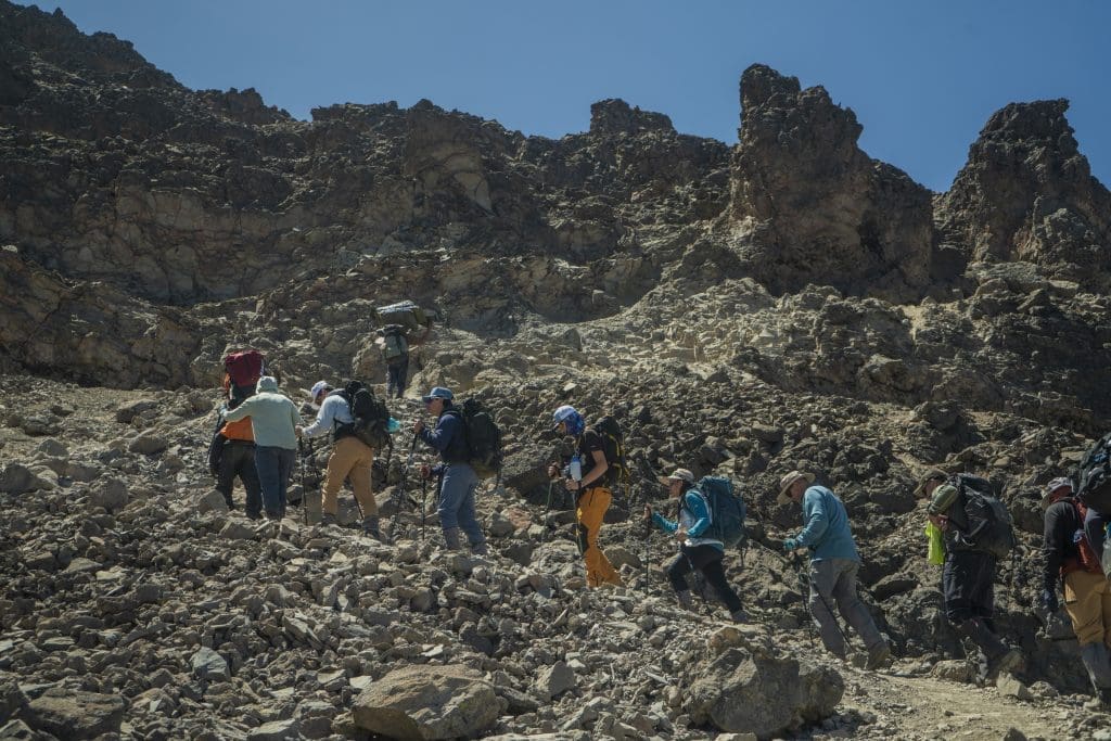 Group of climbers ascending a steep rocky trail in Mount Kilimanjaro’s alpine desert zone using trekking poles.