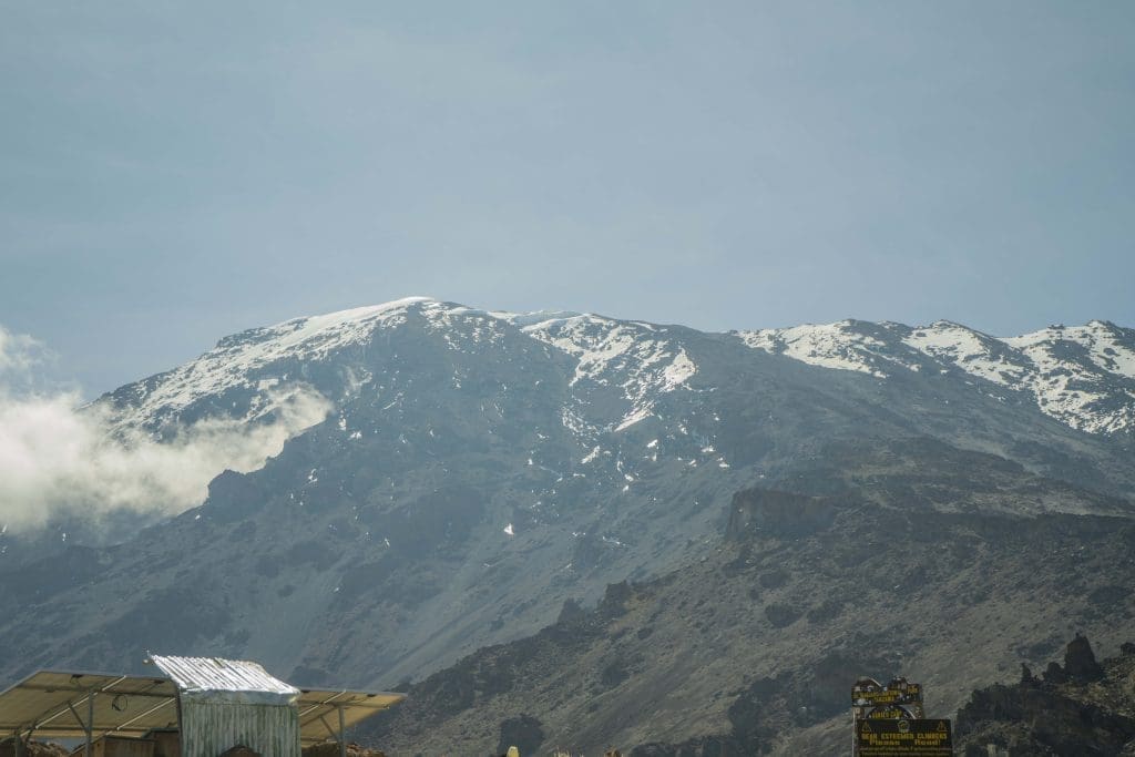 Snow-covered summit of Mount Kilimanjaro with clouds forming along the upper slopes, illustrating cold weather conditions at high altitude.
