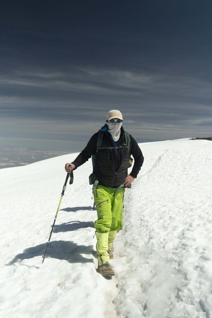 Climber trekking across snow near the summit of Mount Kilimanjaro using a walking pole at high altitude.