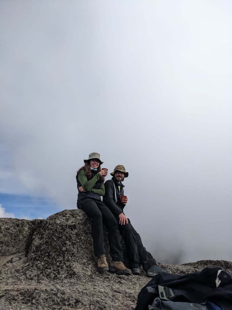 Trekkers taking a tea break on a rocky section of the Lemosho Route with clouds surrounding them on Mount Kilimanjaro.