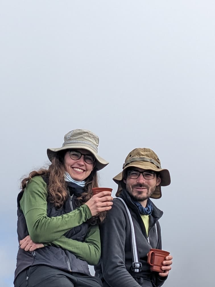 Two climbers smiling while enjoying hot drinks during a rest stop on the Lemosho Route of Mount Kilimanjaro.