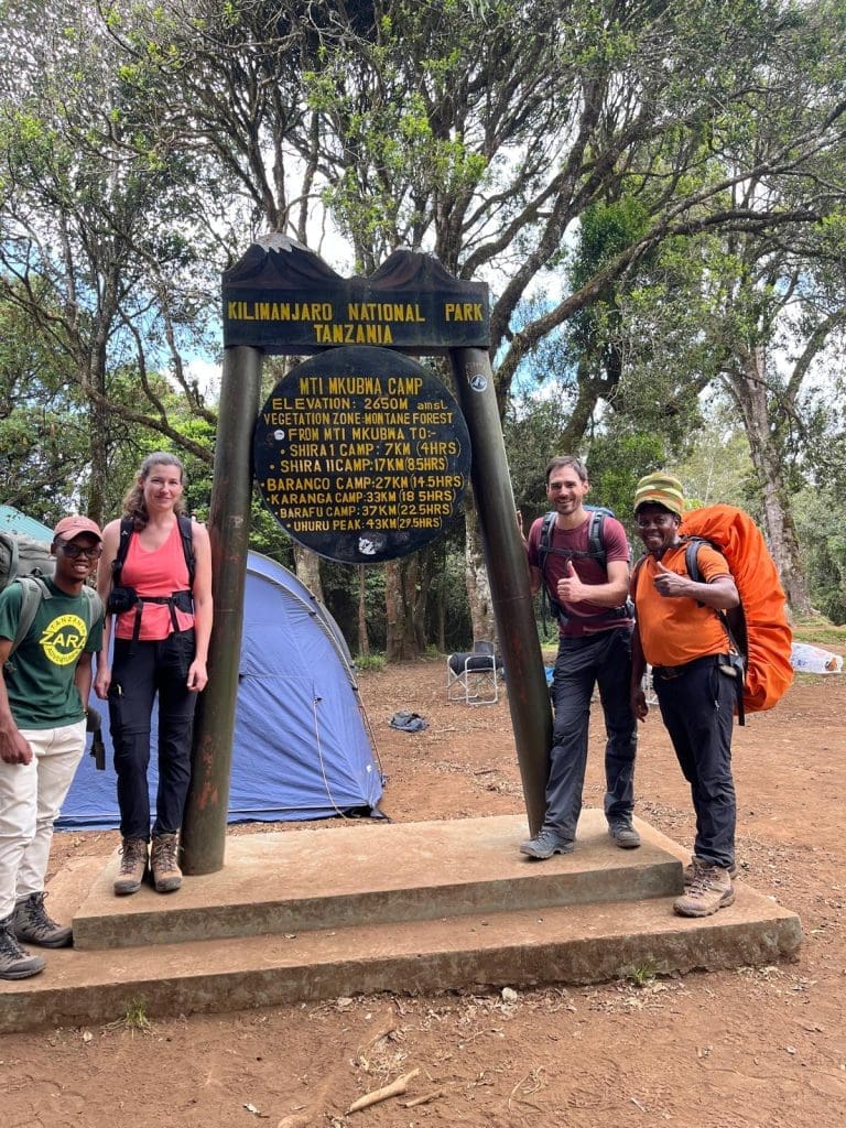 Climbers and a Zara Tanzania Adventures guide at Mti Mkubwa Camp sign on the Lemosho Route, Kilimanjaro National Park.