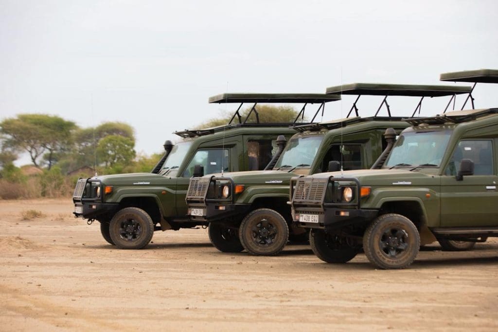 Fleet of 4x4 safari vehicles with pop-up roofs parked in the Tanzanian savannah ready for game drives.