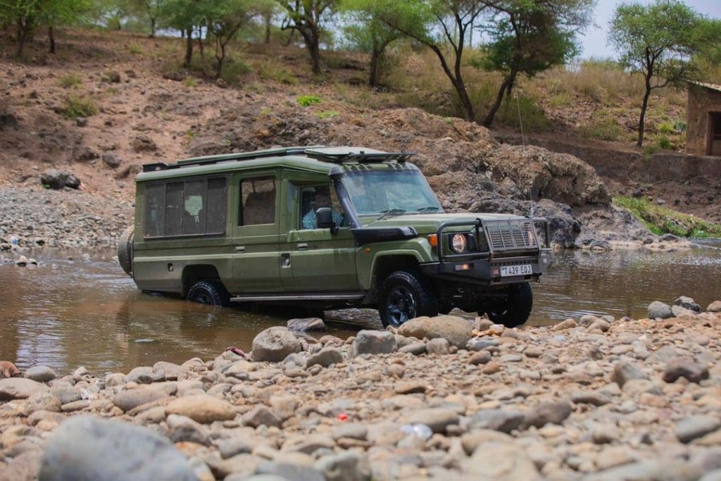 4x4 safari vehicle crossing a shallow river during a game drive in Tanzania.