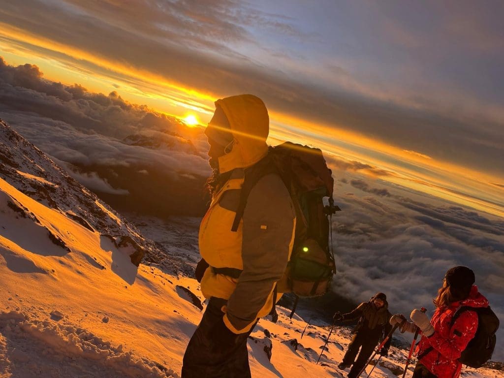 Climbers trekking above the clouds at sunrise near the summit of Mount Kilimanjaro during the final ascent.